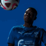 Asisat Oshoala in Al Hilal jersey during her unveiling, controlling a ball against a blue background