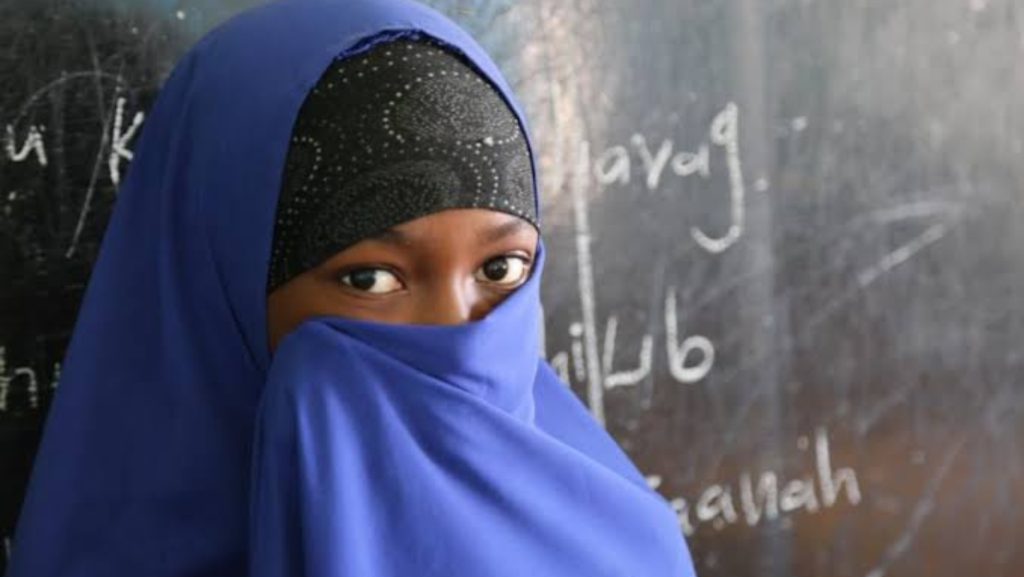 A young Nigerian girl in school uniform stands in a rural setting, symbolizing the child marriage crisis persisting in Nigeria despite new laws and Sharia challenges, October 2025.
