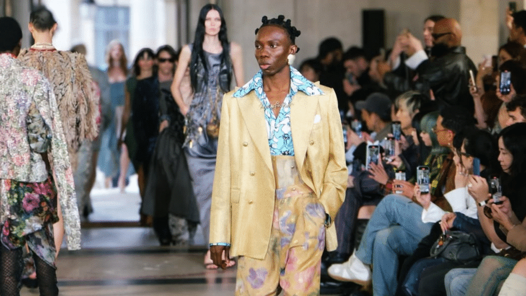 Blaqbonez, the Nigerian rapper, commands the runway at Paris Fashion Week Spring/Summer 2026 in a standout cream double-breasted suit layered over a colorful abstract-printed shirt, with matching wide-leg pants and chunky black loafers.